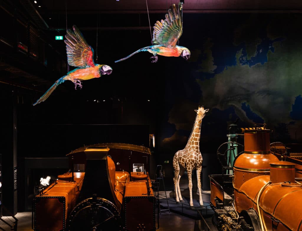 exposition animalia sculptures d'animaux au milieu des trains deux perroquets une girafe